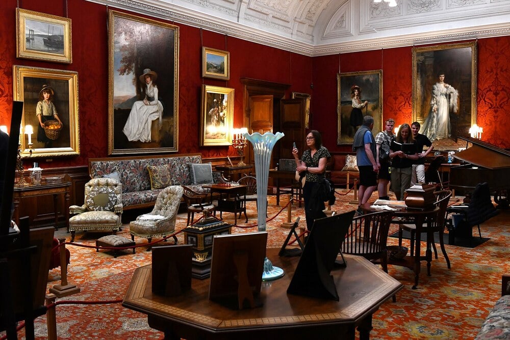 A lavish historic music room with antique furniture, portraits, and red walls.