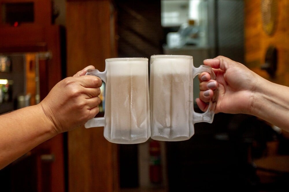Two people clink frosty beer mugs in a toast.