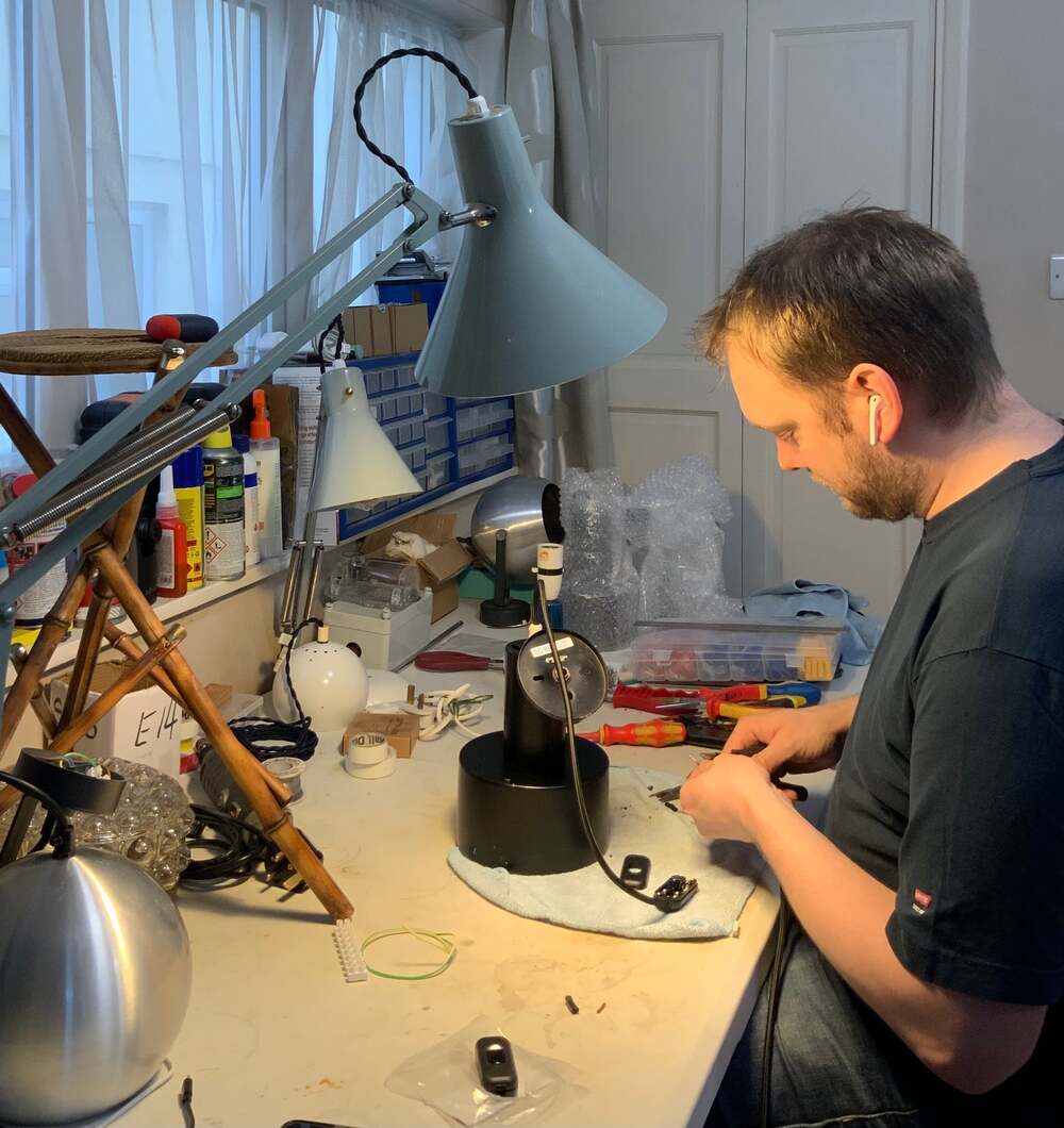 A person repairing electronics under a desk lamp.