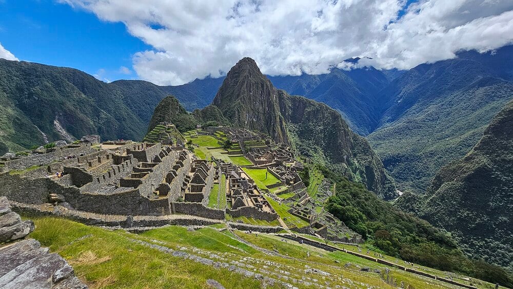 The ancient stone ruins of Machu Picchu on a green Andean mountain ridge.