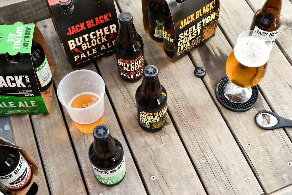 An assortment of beer bottles, packs, and glasses arranged on a wooden table.