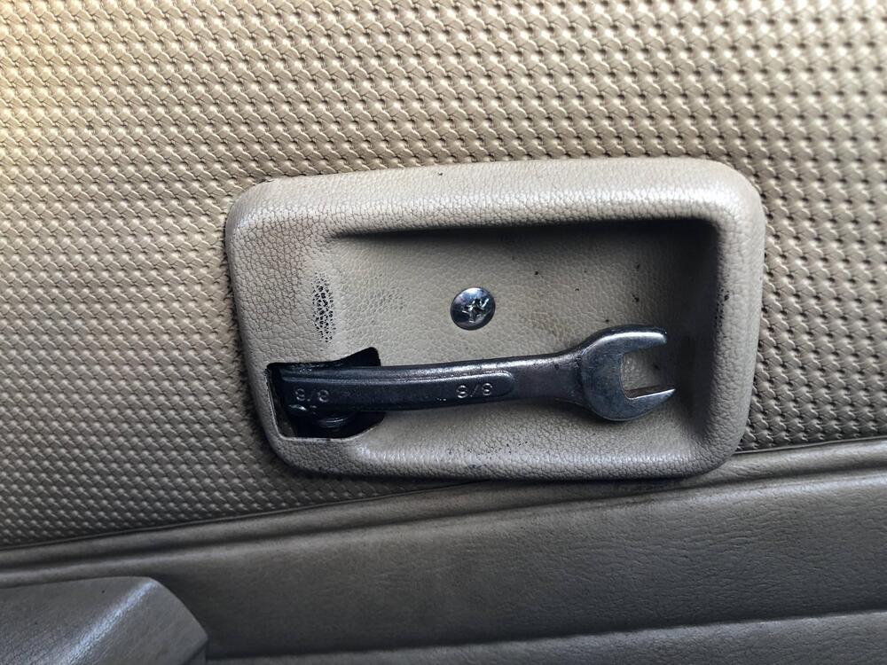 A wrench is used as an improvised car door handle, secured inside a beige car door panel.