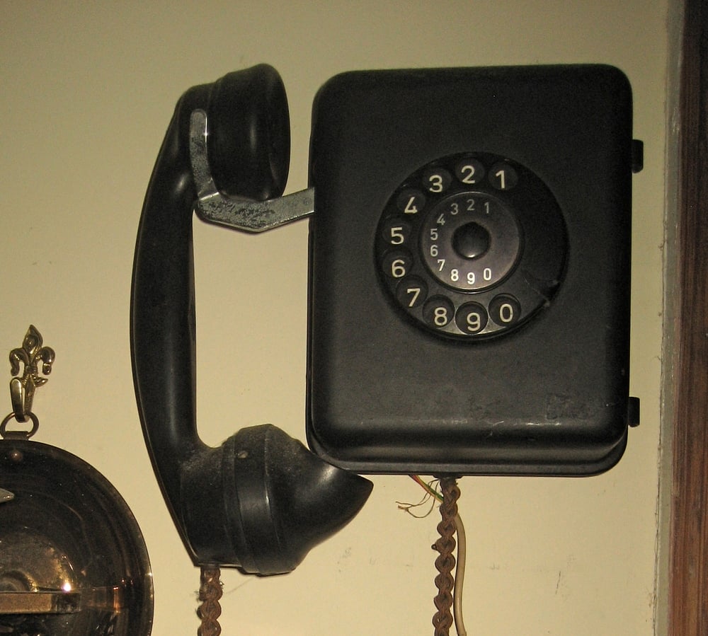 A vintage black rotary telephone mounted on a wall.