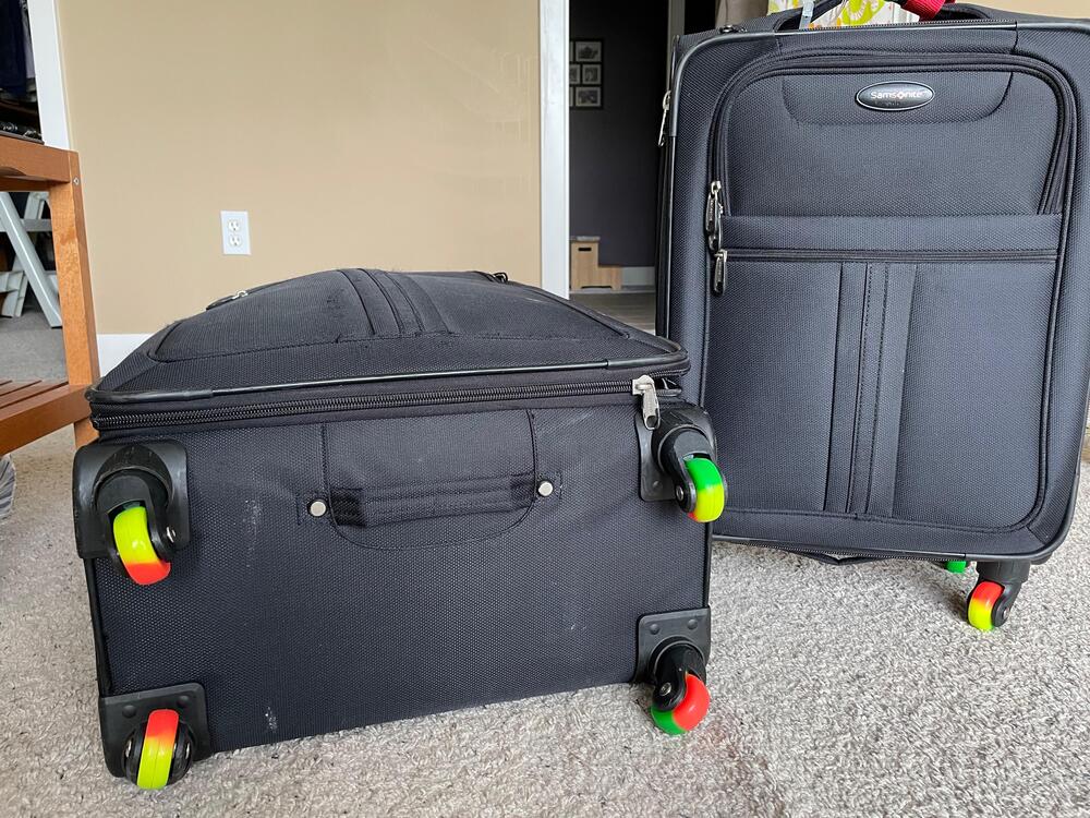 Two black suitcases, one upright and one lying on its side, both with colorful red, green, and yellow wheels, are placed on a carpeted floor in a room with beige walls.