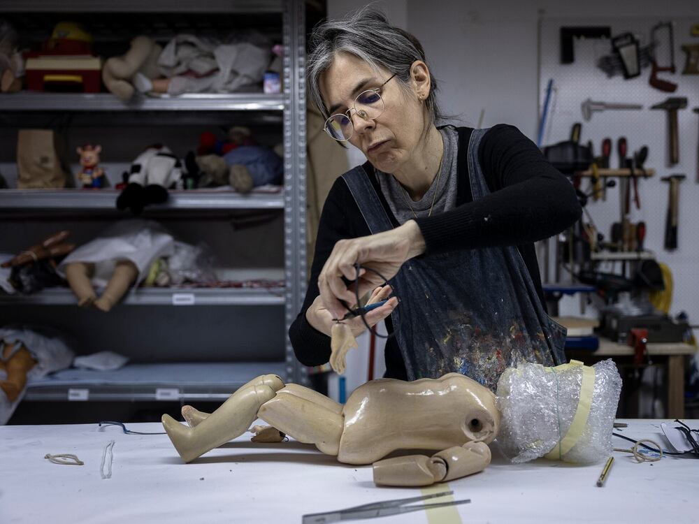 A craftsperson repairing a wooden doll at a workbench.