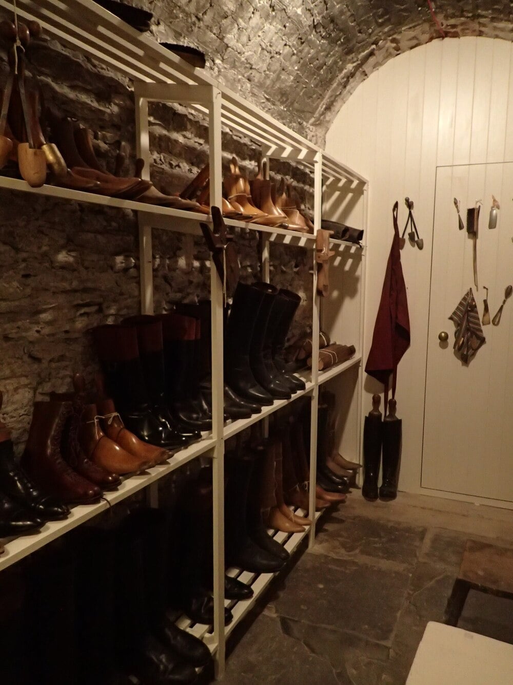 A historic boot room with stone walls and shelves filled with boots and shoes.