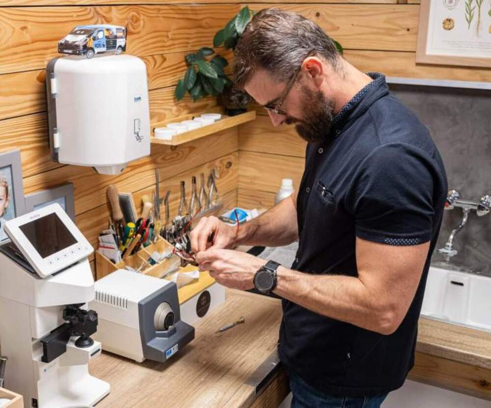 A person repairing eyeglass frames at an optical workbench.