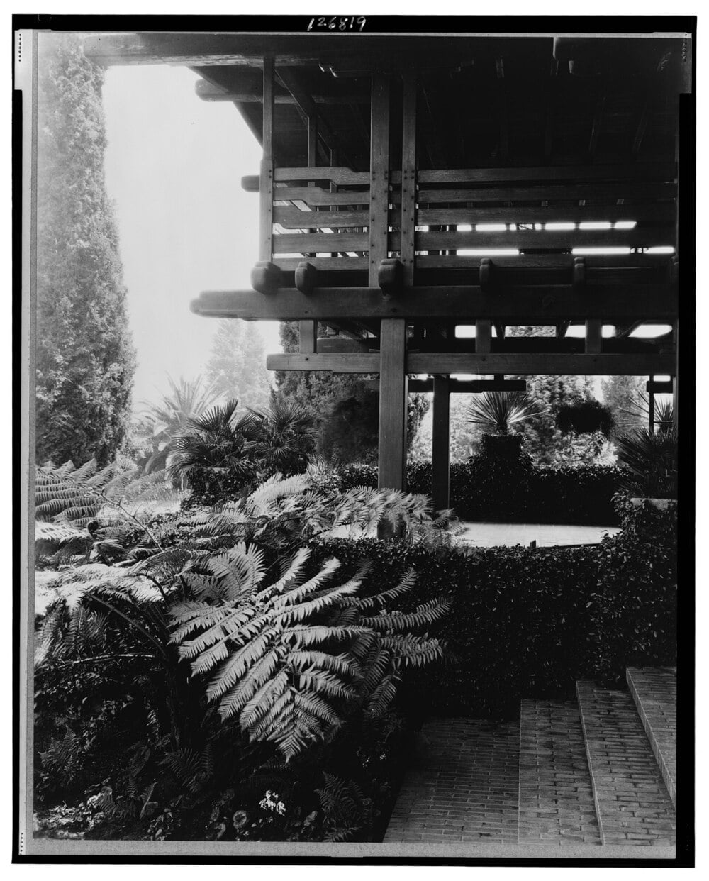 A historic house with a covered sleeping porch surrounded by lush landscaping.