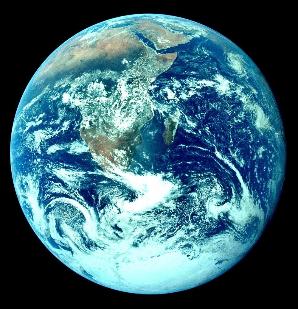 Photo of Earth from space showing Africa, the Middle East, and parts of Asia, with swirling white clouds over blue oceans and green-brown landmasses on a black background.