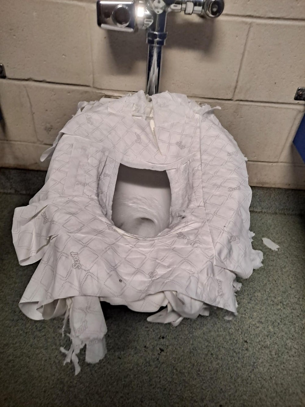 A public toilet with excessive layers of toilet seat covers and toilet paper covering the seat, making it look messy and overflowing.