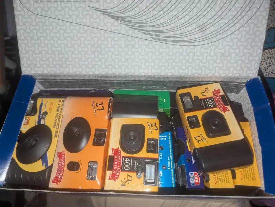 An open box containing several Kodak disposable cameras, mostly yellow and black, arranged neatly side by side.