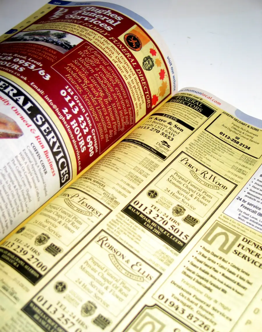 An open phone book showing yellow pages with business advertisements and contact information, mainly for funeral services. The pages are filled with text, logos, and boxes highlighting different companies.