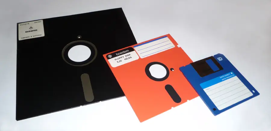 Three floppy disks of different sizes (8-inch black, 5.25-inch orange, and 3.5-inch blue) are arranged side by side on a white surface.
