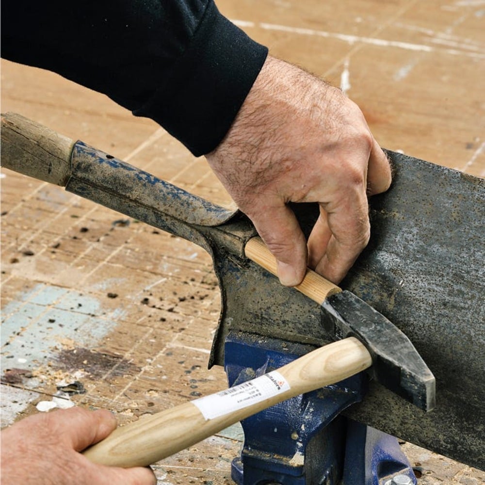 A person repairing a farm tool at a workbench.