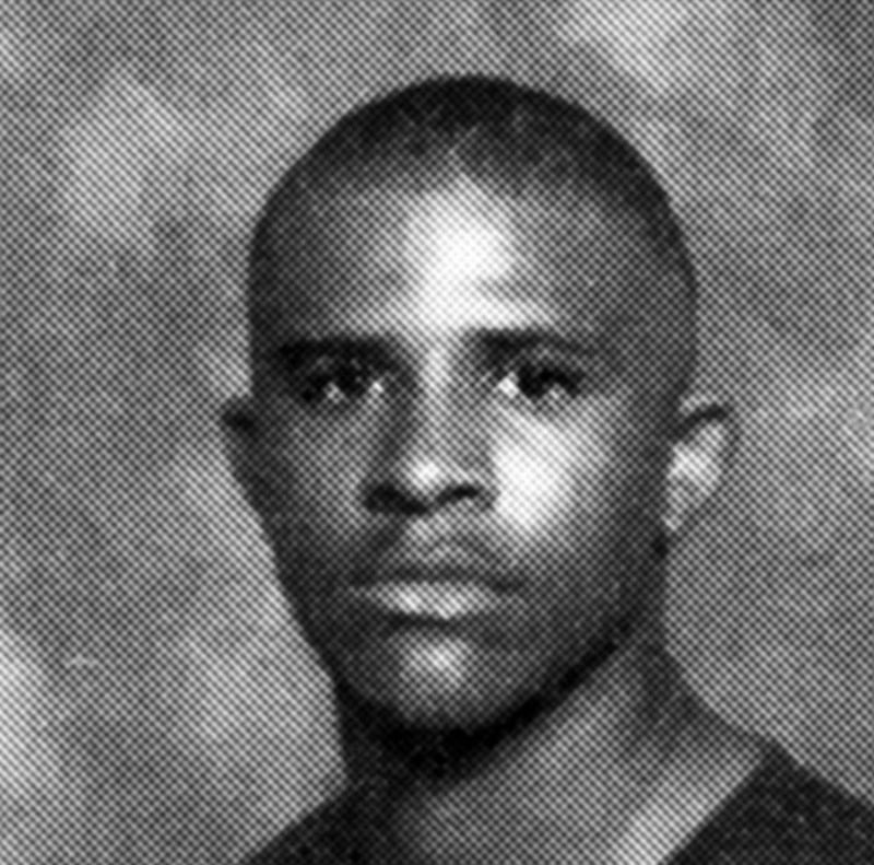 A black and white, grainy portrait of a young person with short hair, looking directly at the camera with a neutral expression against a simple, textured background.