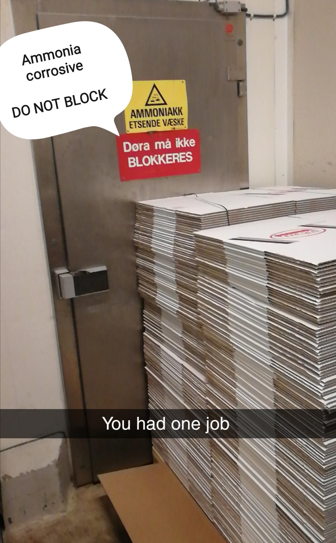 A stack of flat boxes blocks a door labeled “Ammonia corrosive, DO NOT BLOCK,” with a Snapchat caption at the bottom reading, “You had one job.”