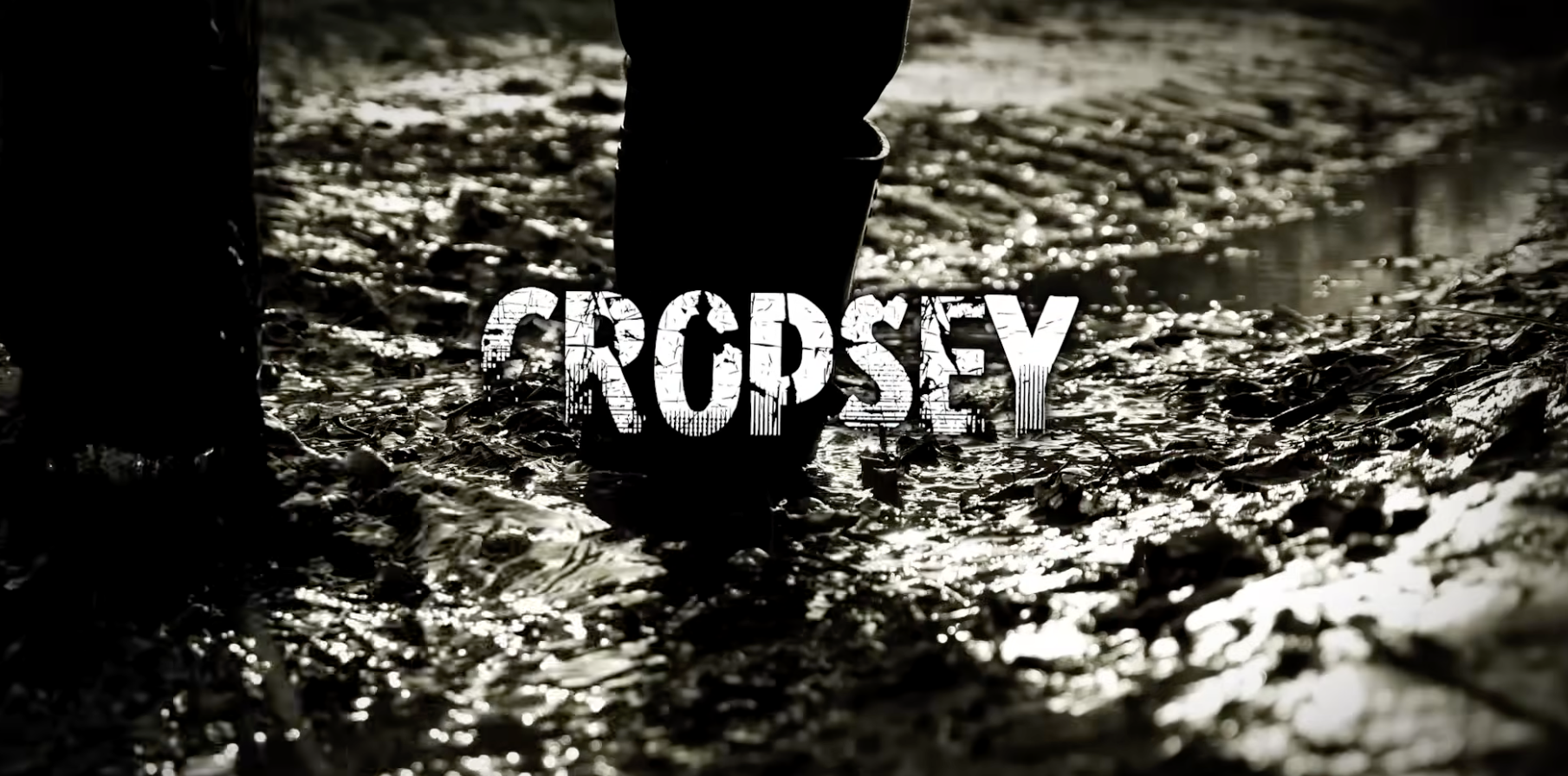 A person stands in muddy water, wearing boots. The ground is deeply rutted, and the word “CROPSEY” appears in bold, distressed white text across the center. The image is in black and white.