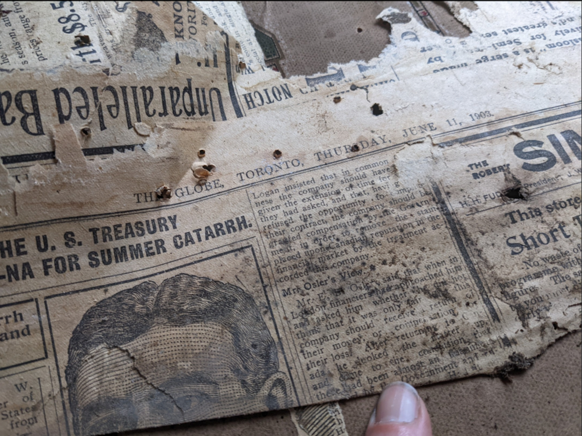 A close-up of a torn, old newspaper dated Thursday, June 11, 1908, with yellowed paper, visible holes, and a person’s finger at the bottom right corner holding the page.
