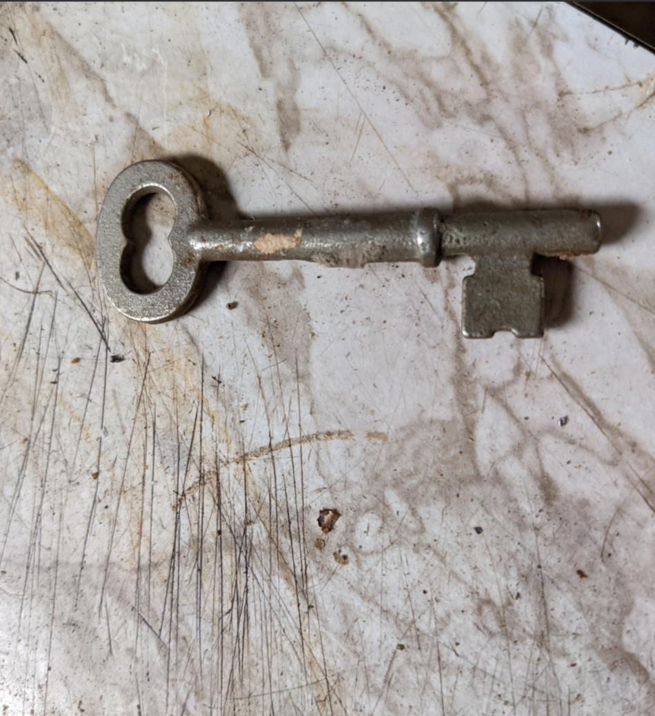 A vintage metal skeleton key rests on a scratched, stained marble or stone surface.