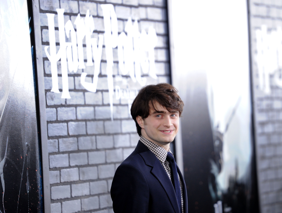 A man in a suit stands smiling in front of a “Harry Potter” movie poster on a brick wall background at an event or premiere.