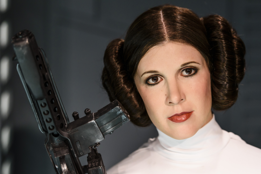 A woman in a white outfit with brown hair in side buns holds a futuristic blaster, standing against a sci-fi background.