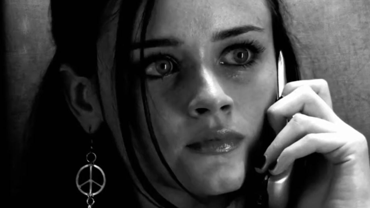A young woman with wide eyes holds a phone to her ear. She wears a peace sign earring and looks serious or worried. The image is in black and white.