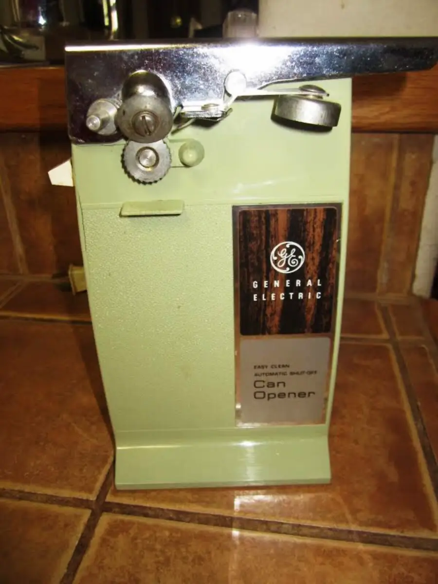 A vintage General Electric electric can opener in avocado green with chrome and wood accents, sitting on a tiled kitchen counter.