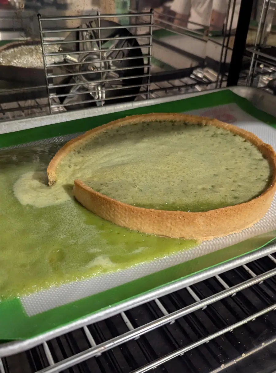 A baking tray with a tart crust, but the green filling has leaked and spread across the tray, overflowing beyond the crust.
