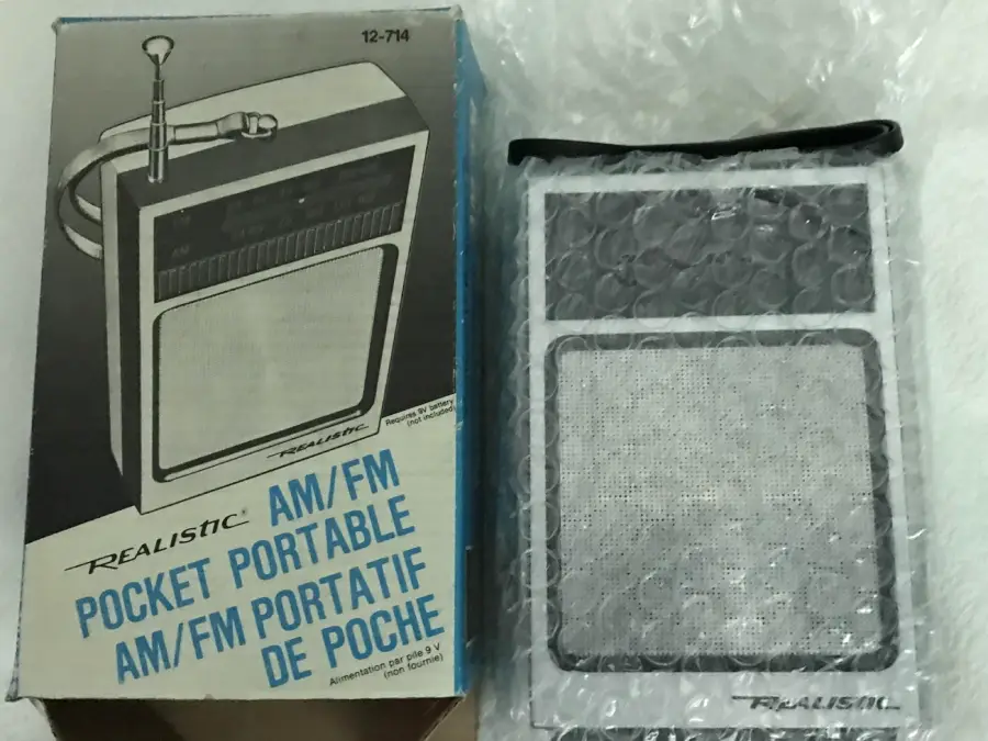 A vintage Realistic pocket AM/FM radio in bubble wrap is next to its original box, which is labeled in English and French and shows an illustration of the radio and its antenna.