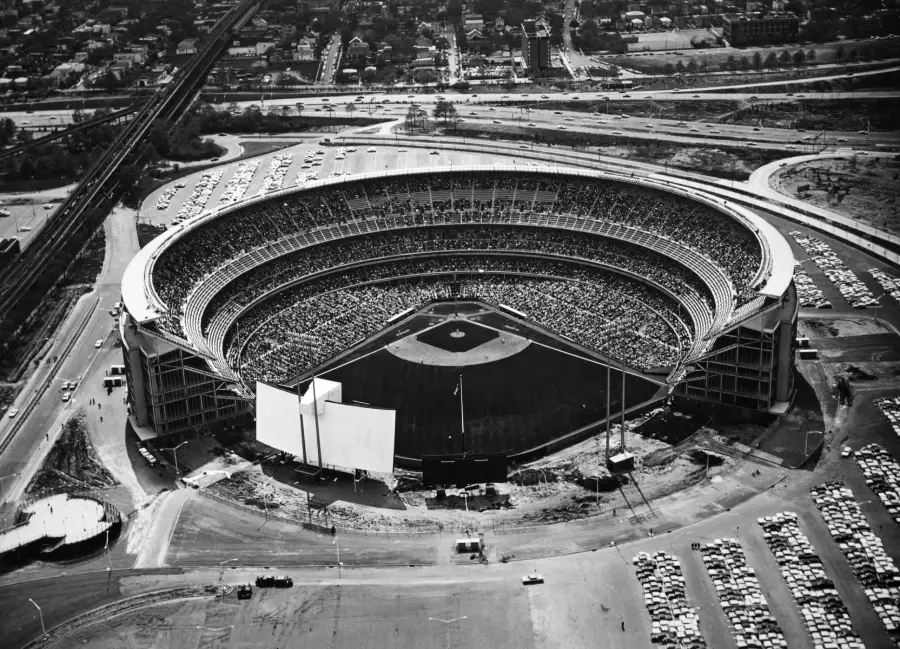 Aerial view of a baseball stadium filled with spectators, surrounded by parking lots and roads, in a black and white image.