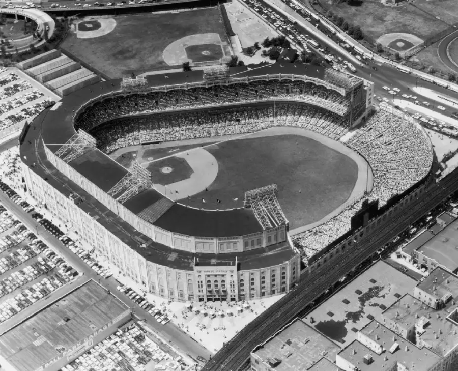 Aerial black and white view of Yankee Stadium packed with fans during a baseball game, surrounded by parking lots, roads, and nearby buildings.