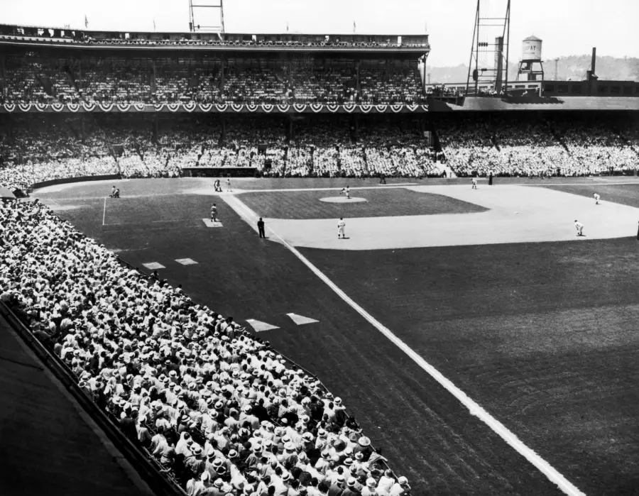 Black-and-white photo of a crowded baseball stadium during a game, with fans filling the stands, bunting decorations, and players positioned on the field.