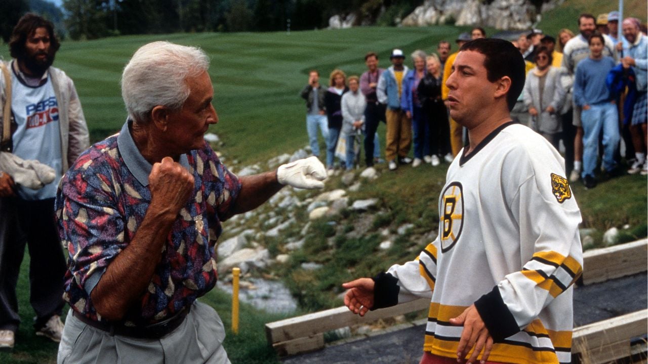 An older man in golf attire raises his fist as if to fight a younger man wearing a hockey jersey, with a crowd watching on a golf course in the background.