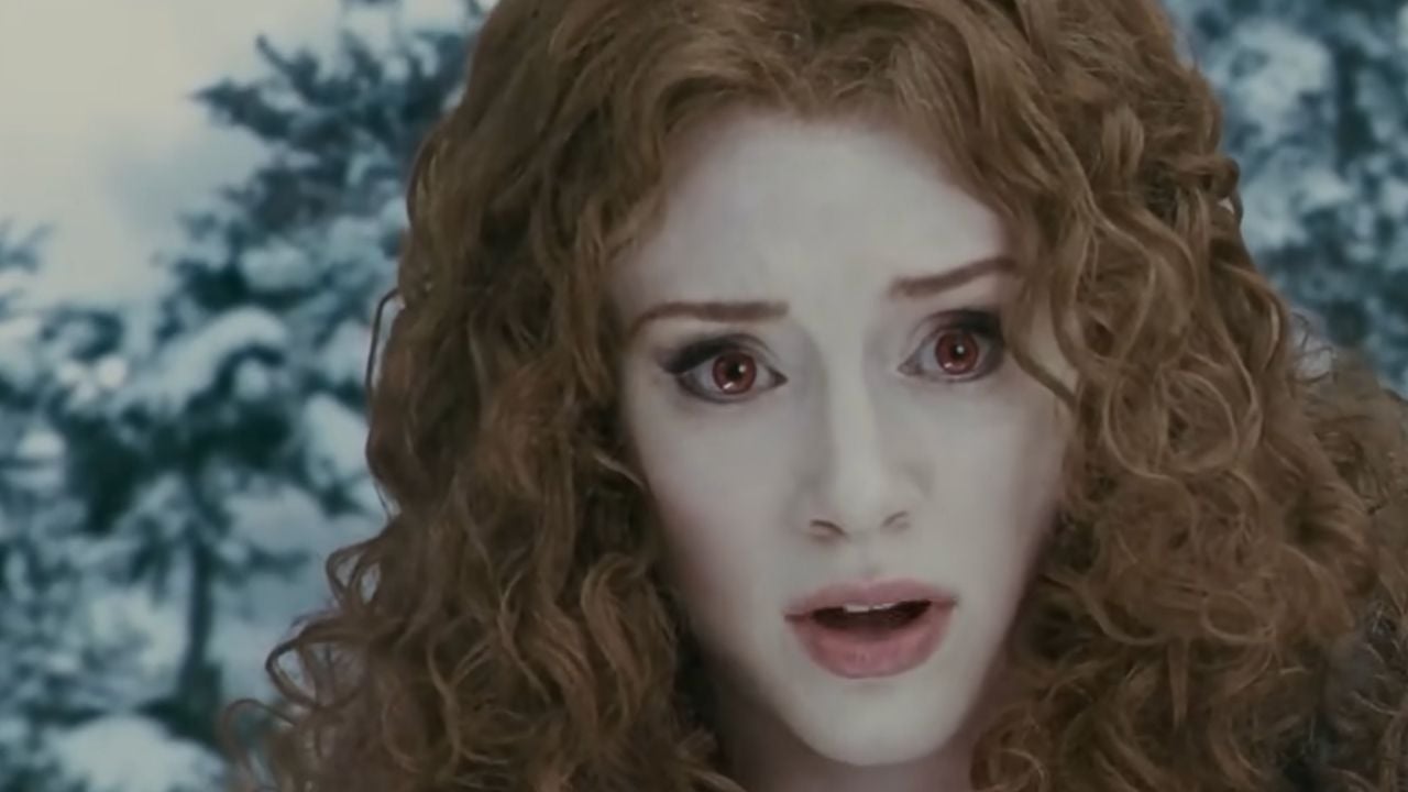 A woman with pale skin, curly red hair, and red eyes looks forward with a surprised expression. Snow-covered trees are blurred in the background.