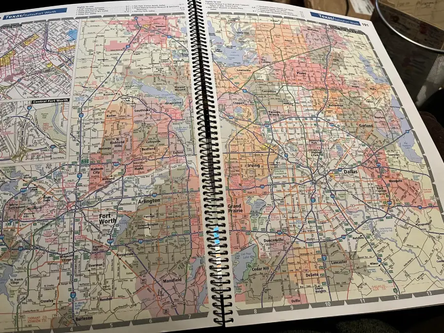 A spiral-bound atlas is open to detailed color maps of the Dallas–Fort Worth area in Texas, showing roads, highways, and city names with labeled regions and points of interest.