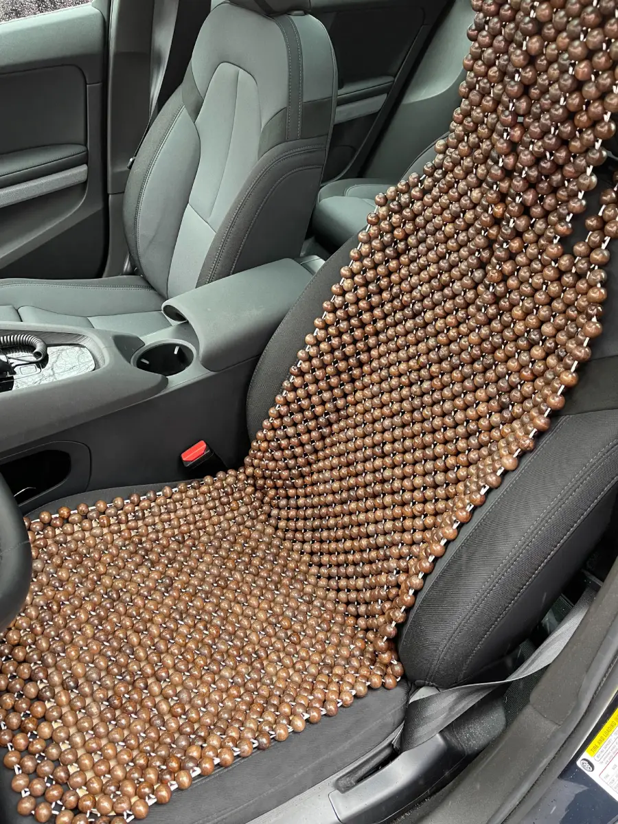 A car seat covered with a brown wooden bead seat cover, designed for comfort and ventilation, placed on the driver’s seat in a modern car interior.