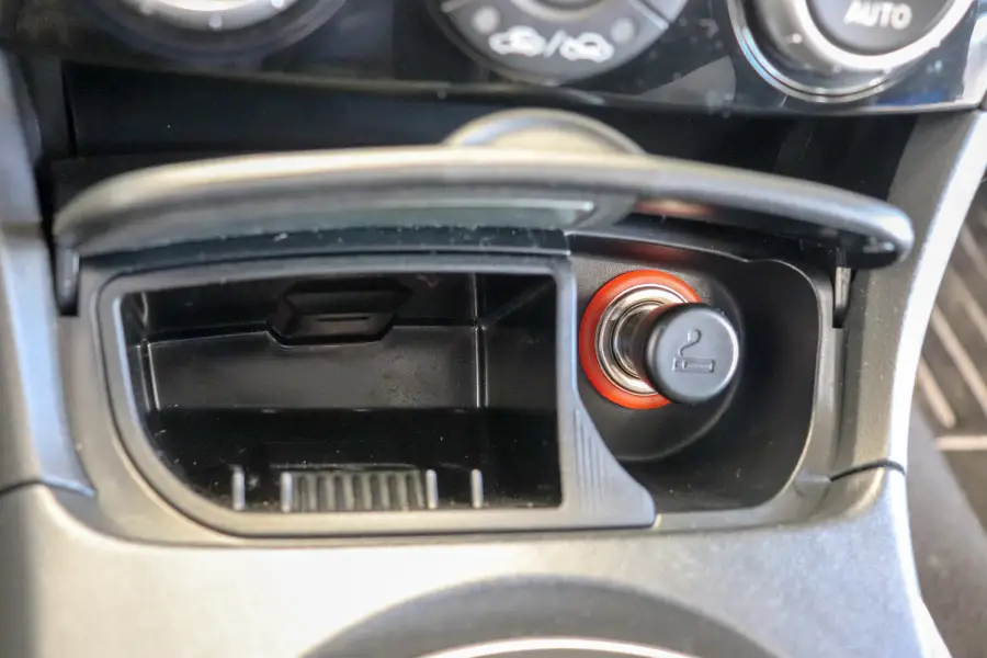 Close-up of a car’s dashboard showing an open storage compartment and a cigarette lighter socket with a red ring and lighter symbol.