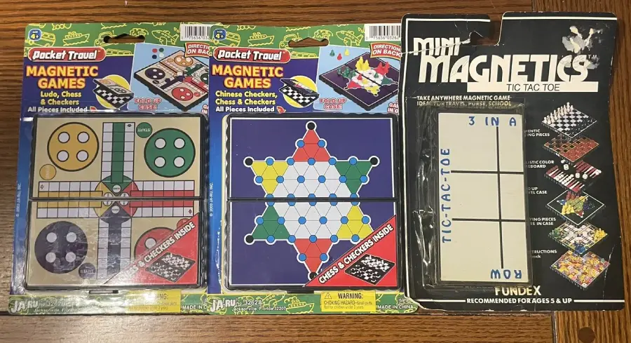 Three packages of pocket travel magnetic games: Ludo, Chess & Checkers; Chinese Checkers, Chess & Checkers; and a FunDex Mini Magnetics Tic-Tac-Toe set. All are displayed on a wooden surface.