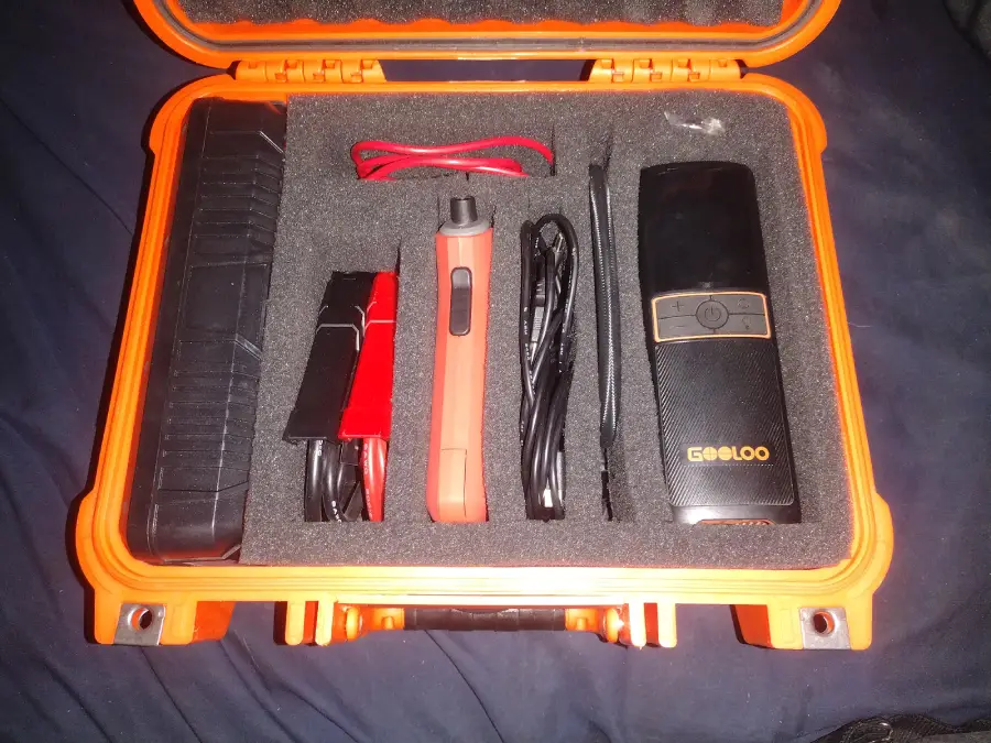 An orange hard case with foam inserts holds a jump starter kit, including a battery pack, clamps, cables, a tool, and a GOOLOO-branded device.