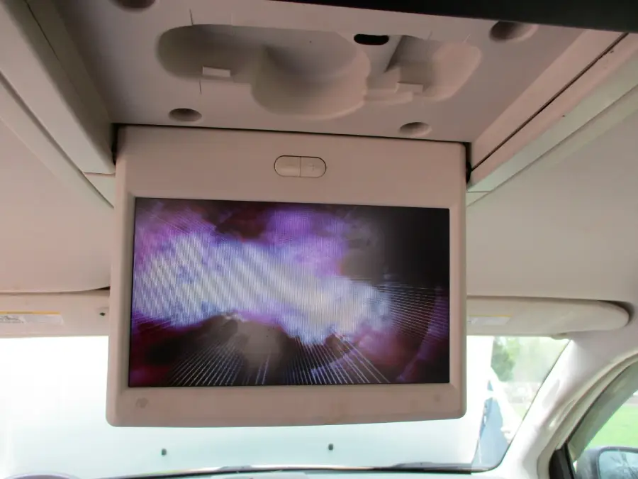 Ceiling-mounted flip-down screen in a vehicle displaying a colorful, abstract image with purple and white hues.