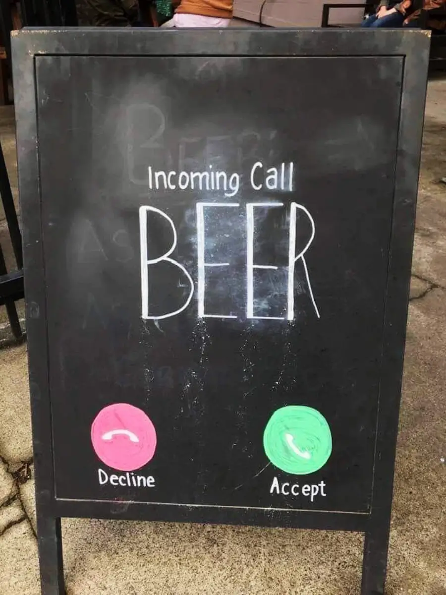 A chalkboard sign reads “Incoming Call BEER” with red “Decline” and green “Accept” icons, mimicking a phone call screen, on a sidewalk outside a venue.