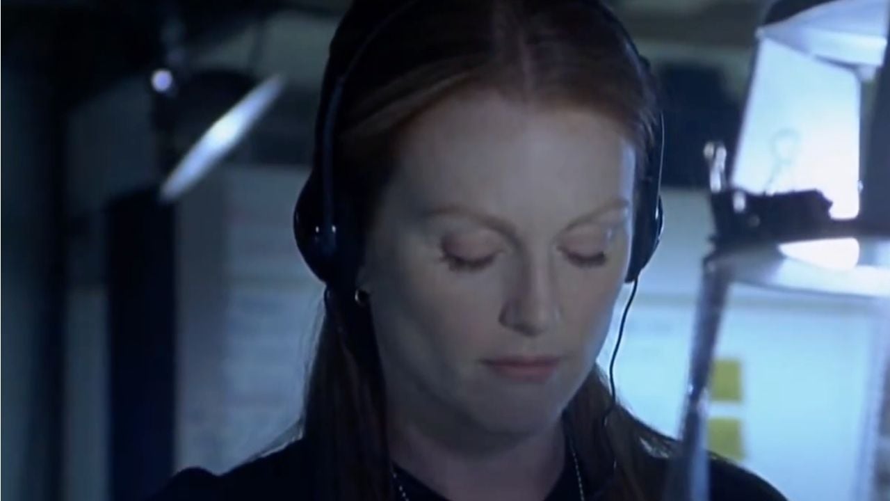 A woman with red hair wearing headphones looks down thoughtfully in a dimly lit room with blue tones.