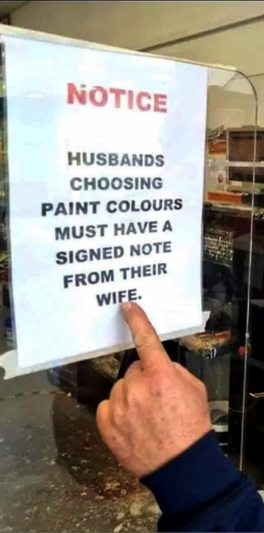A hand points to a humorous sign on a window that reads, “Husbands choosing paint colours must have a signed note from their wife.”