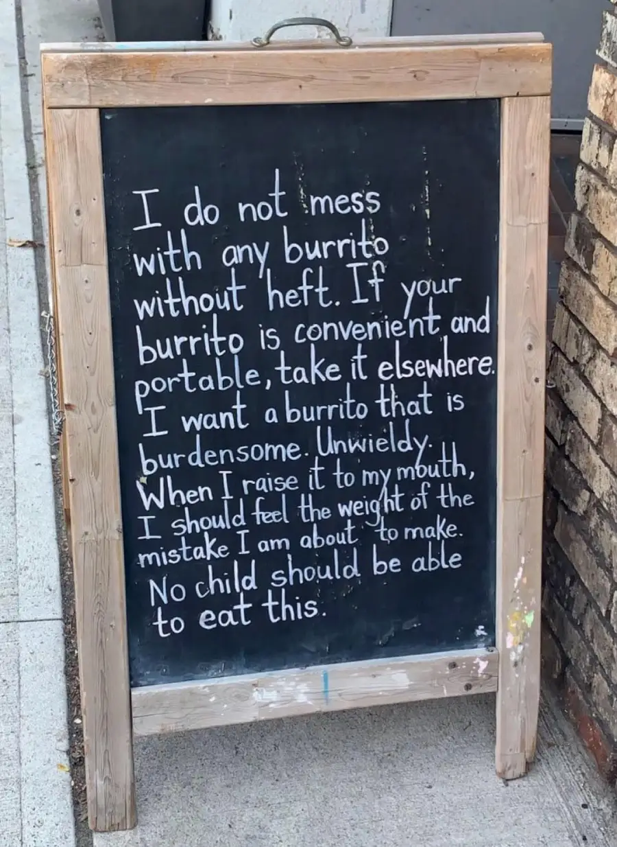 A chalkboard sign reads: “I do not mess with any burrito without heft. If your burrito is convenient and portable, take it elsewhere. I want a burrito that is burdensome. Unwieldy. When I raise it to my mouth, I should feel the weight of the mistake I am about to make. No child should be able to eat this.”