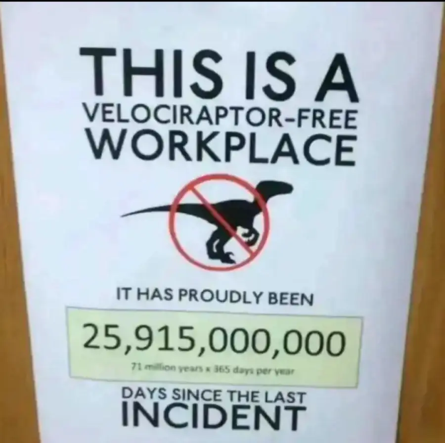 A sign reads “This is a velociraptor-free workplace.” Below a crossed-out velociraptor, it says, “It has proudly been 25,915,000,000 days since the last incident.”