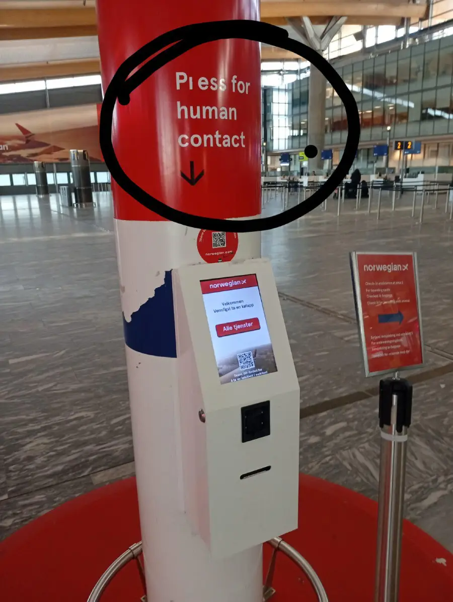 A kiosk at an airport with a sign reading “Press for human contact” and an arrow pointing down, with the word “Press” misspelled as “Pless.” There is a touchscreen and directions for use.