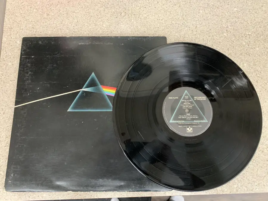 A vinyl record partially out of its sleeve featuring Pink Floyd’s “The Dark Side of the Moon” album with the iconic prism and rainbow cover art, placed on a light-colored countertop.