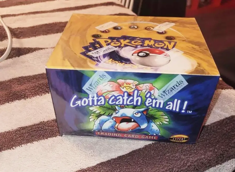 A sealed Pokémon trading card game booster box with Venusaur artwork and the slogan “Gotta catch ’em all!” displayed on the front, placed on a striped towel.