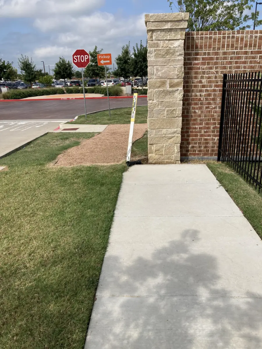 A sidewalk ends abruptly at a brick wall, with a patch of gravel and a stop sign visible nearby. The sidewalk provides no clear path forward.