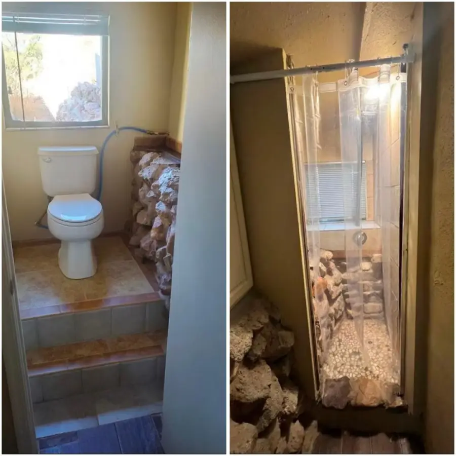 A bathroom with a toilet and shower surrounded by rocks; the shower has a clear curtain and a stone floor, and both areas have a natural, rustic design.